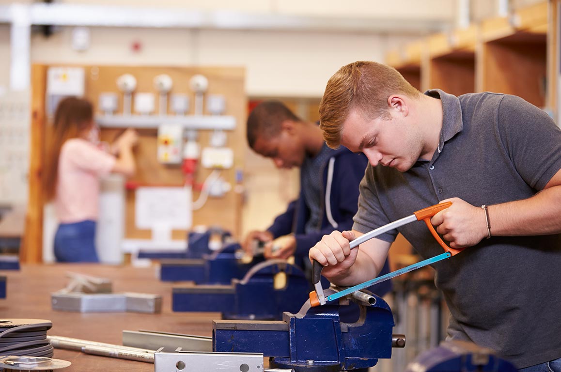 A young male college student cutting piping on an electrical apprenticeship